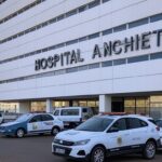 Exterior do Hospital Anchieta em Brasília com viaturas policiais, representando investigação de mortes suspeitas e prisões por injeções irregulares.
