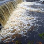 Reservatório do Descoberto transbordando no DF, com água inundando áreas próximas, expondo riscos de falhas no abastecimento.
