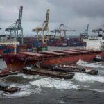 Navio Wisdom Venture colidido com balsas no Porto de Santos, com danos e mar agitado, em estilo fotojornalístico.