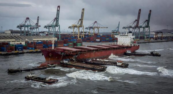 Navio Wisdom Venture colidido com balsas no Porto de Santos, com danos e mar agitado, em estilo fotojornalístico.