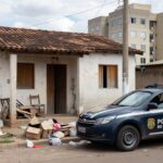 Viatura da Polícia Civil do DF em frente a casa residencial em Brasília, porta aberta e itens espalhados, representando caso de criança sozinha com drogas.