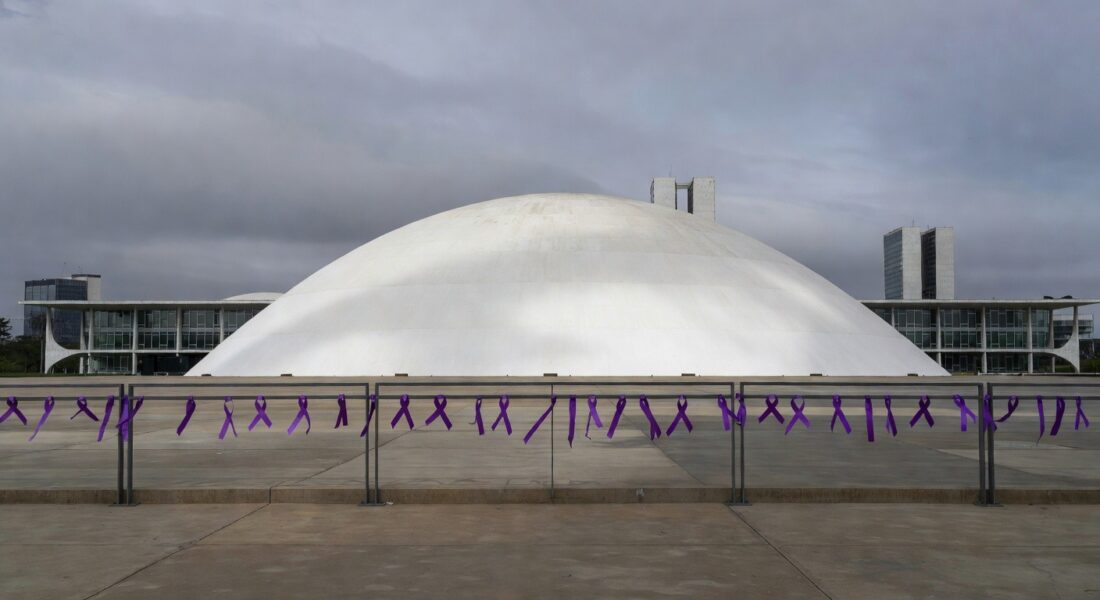 Edifício da CLDF em Brasília com fitas roxas contra violência de gênero em dia nublado.