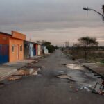 Vista de rua em Riacho Fundo I com bandeiras de aniversário e deficiências urbanas como buracos e lixo, no DF.