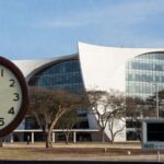 Edifício da Câmara Legislativa do DF em Brasília com relógio parado e monitor cardíaco, simbolizando lentidão em lei para ecocardiograma em bebês com Down e riscos cardíacos.