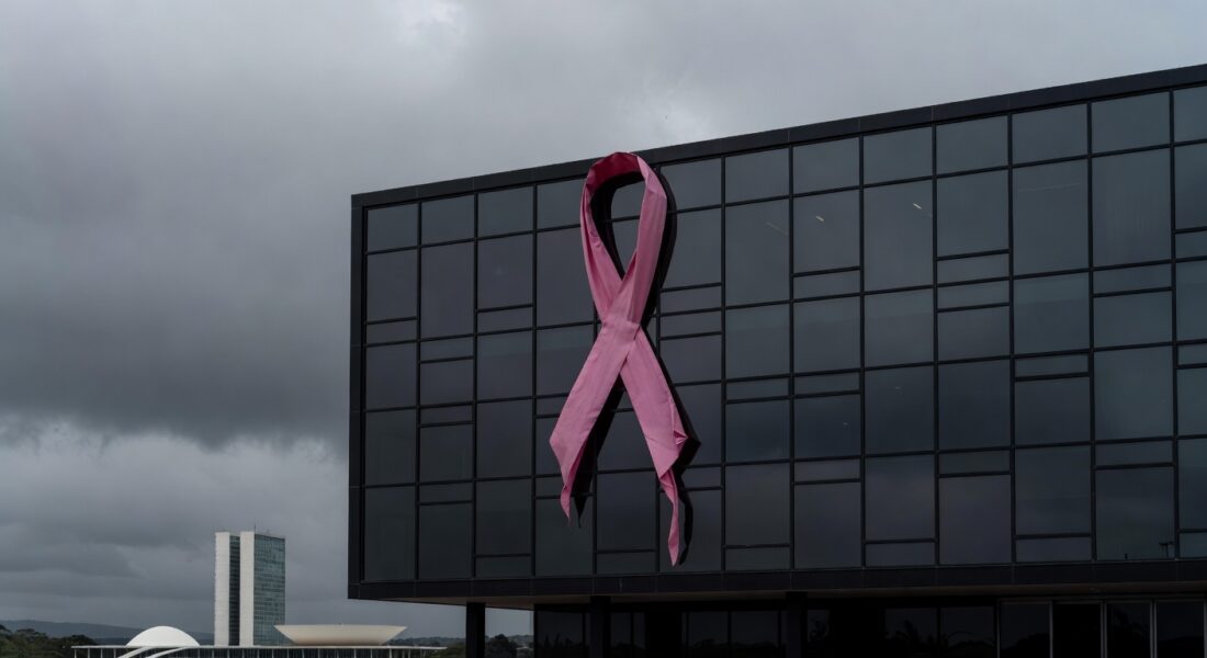 Fachada da Câmara Legislativa do DF com laço rosa desleixado, destacando lacunas no apoio a vítimas de câncer de mama.