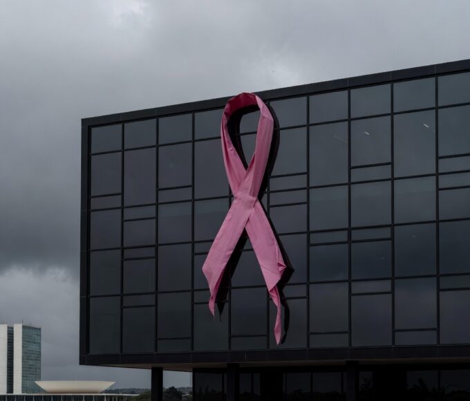 Fachada da Câmara Legislativa do DF com laço rosa desleixado, destacando lacunas no apoio a vítimas de câncer de mama.