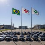 Cerimônia de formatura da PMDF em Brasília, com viaturas policiais e bandeiras ao fundo.