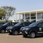 Mesa oficial com decreto de promoção de policiais militares no Palácio do Buriti, Brasília, com viaturas da PMDF ao fundo.