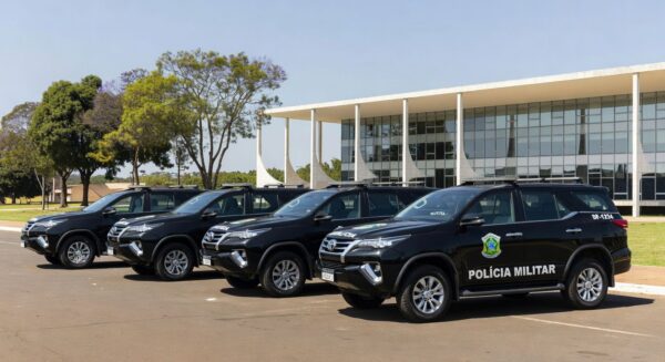Mesa oficial com decreto de promoção de policiais militares no Palácio do Buriti, Brasília, com viaturas da PMDF ao fundo.