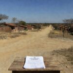 Documentos de regularização fundiária em Planaltina, DF, com casas e terrenos ao fundo.
