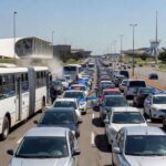 Trânsito congestionado com ônibus e viaturas policiais em avenida de Brasília, ilustrando falhas no transporte e segurança no DF.